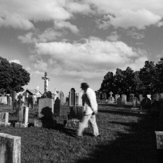 Personne marchant dans un cimetière avec tombes et arbres en arrière-plan.